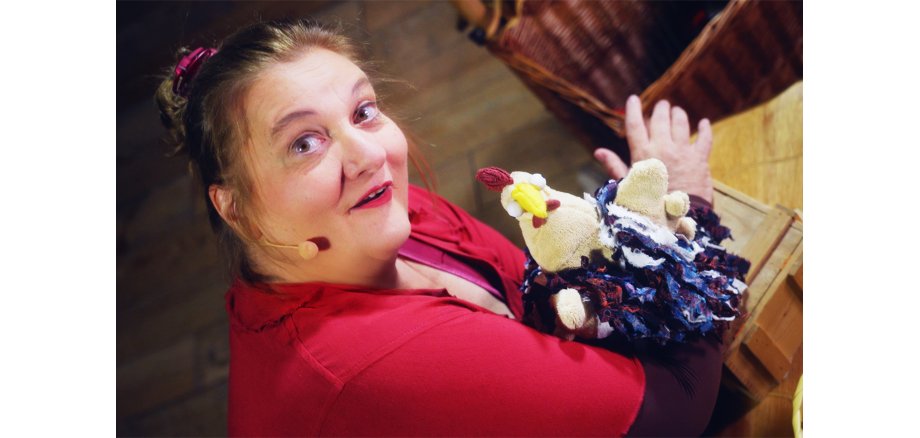 Eine Frau mit roten Kleid hält ein kleines buntes Stoffhuhn in ihrer Hand