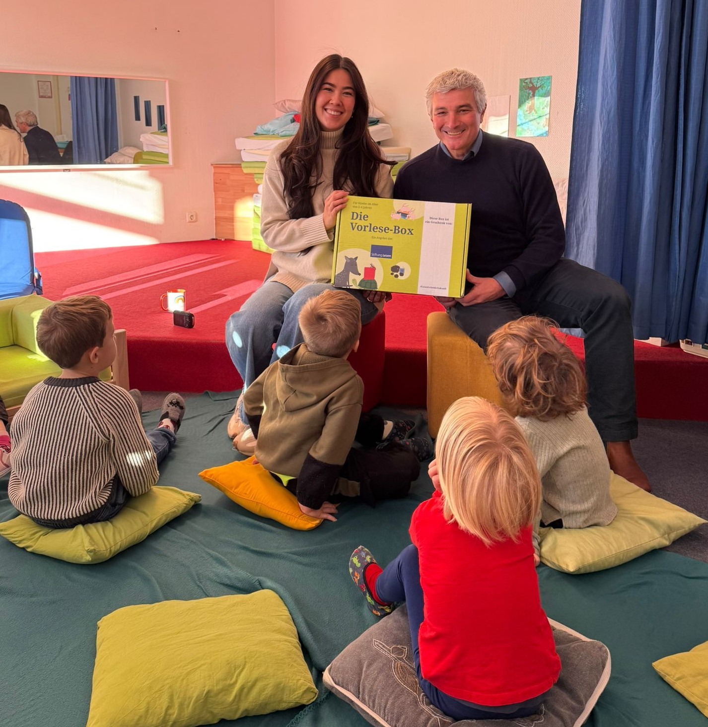 Mann und Frau vor Gruppe von Kindern mit Buch