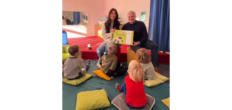 Mann und Frau vor Gruppe von Kindern mit Buch